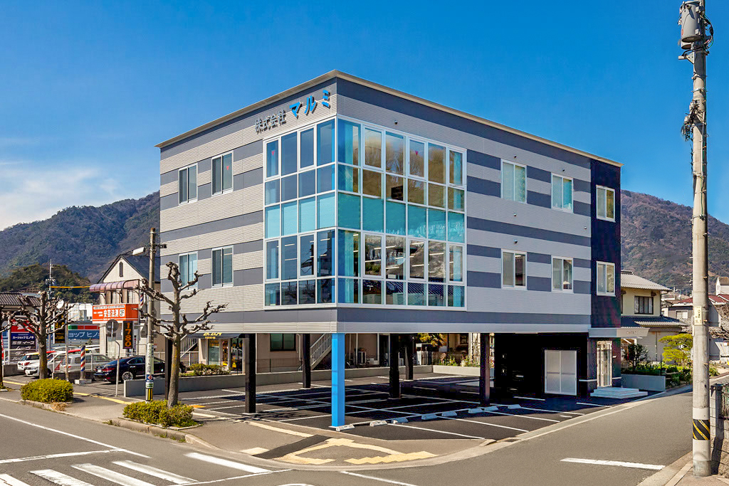 3階建て事務所の外観1。斜めから全景。1階ピロティの柱部分は意匠的なデザインとして1本だけ青い配色になっている。