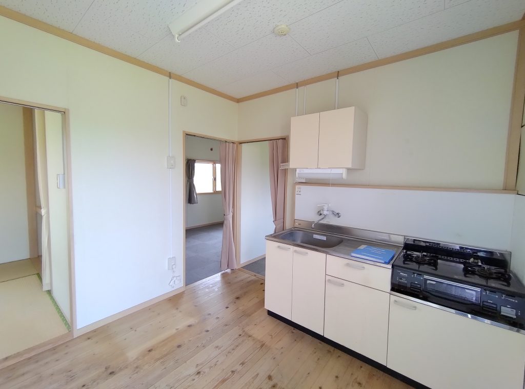 応急仮設住宅の内観1。流し台、コンロ、収納を備えた明るいキッチン。
