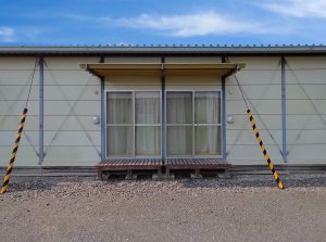 仮設住宅の外観2。建物裏手の正面。掃き出し窓と小さな濡れ縁の様子。