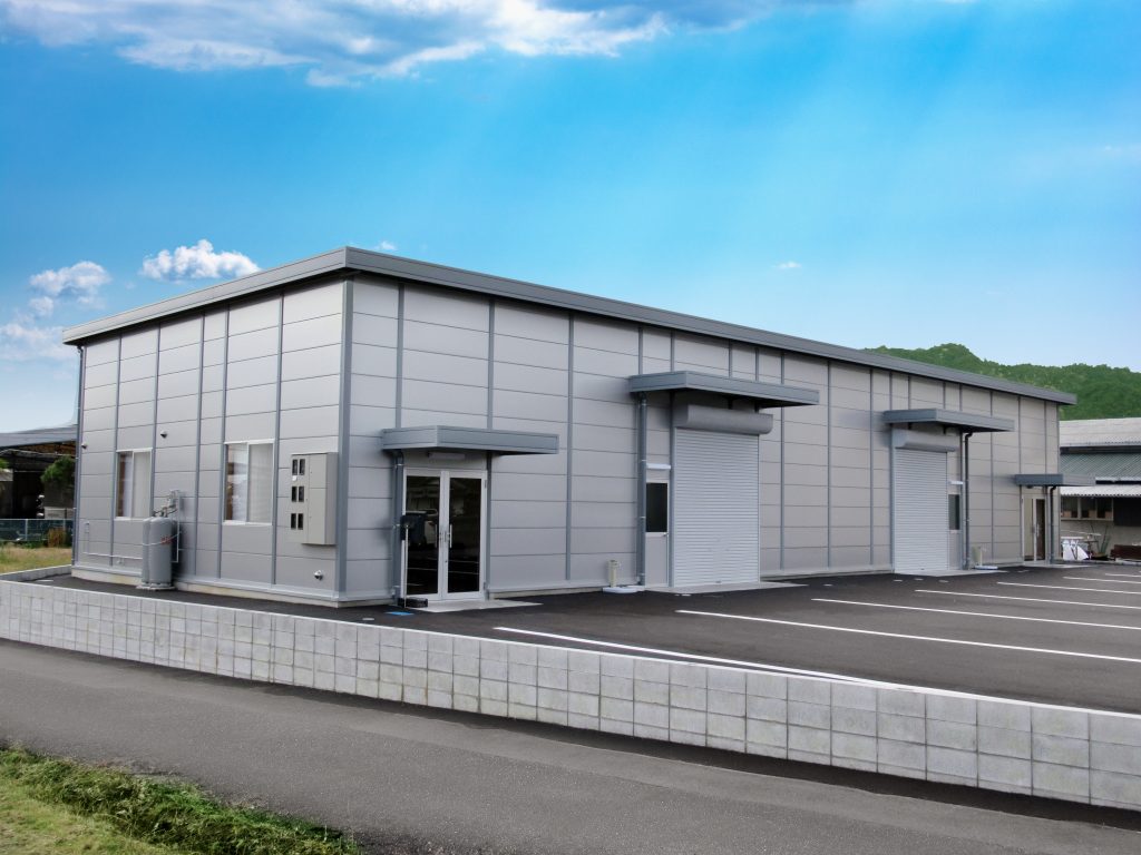 事務所兼倉庫の外観1。斜めからの全景。事務所の玄関と駐車場に面した二つのシャッター開口部の様子。