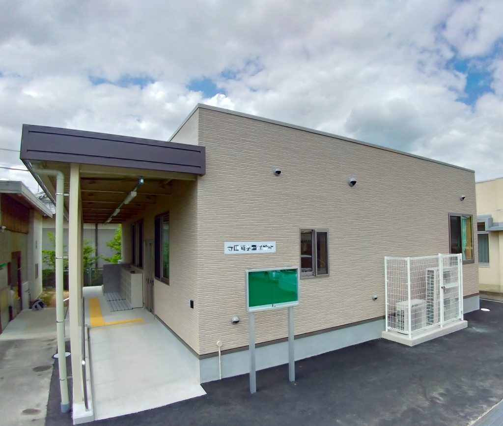 児童クラブの外観1。左斜めから。玄関に続くスロープと手すりは庇に覆われている。