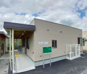 児童クラブの外観1。左斜めから。玄関に続くスロープと手すりは庇に覆われている。