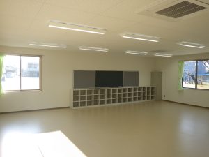 児童クラブの内観1。左斜めから。広々とした室内の後部に黒板と収納棚が配置されている。