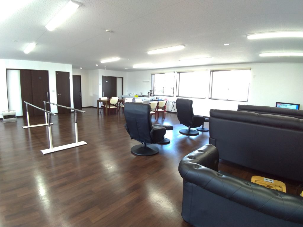 デイサービス施設の内観2。談話室。壁に三か所配された窓から外光が差し込み明るい室内になっている様子。