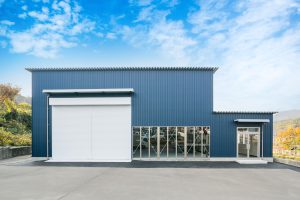 TDシリーズの自動車整備工場・事務所併設棟の正面外観。大開口シャッターとガラス開口で動線と視認性を両立。