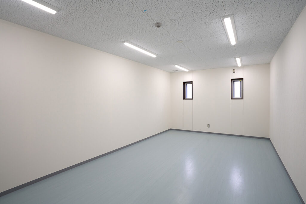 2階建て倉庫兼事務所の男子更衣室内観。入口から写した2枚の縦滑り出し窓。